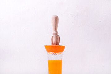 Wooden juicer squeezing orange juice into the drinking glass out of the fruit half against the...