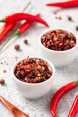 Hot sauce of red dry chili peppers with soy oil in a white bowl close-up.
