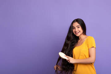Smiling Young Indian Woman Brushing Long Hair With Wooden Comb