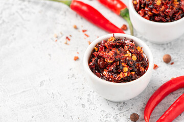 Hot sauce of red dry chili peppers with soy oil in a white bowl close-up.
