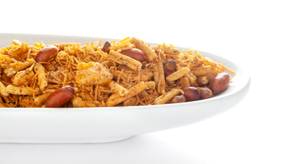 Spicy Chatpata Mixture in a white ceramic bowl made with peanuts, corn flakes, etc. Pile of Indian spicy snacks (Namkeen), under backlight, side view, against the white background.