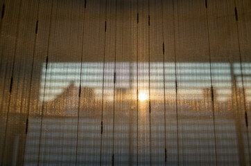 The orange light of the evening sun shines through the sheer curtains.