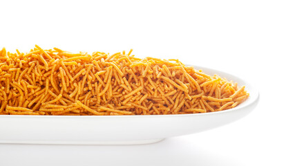 Spicy Aloo Bhujia in a white ceramic oval bowl, made with Red chili, Potatoes, and Chickpeas. Pile of Indian spicy snacks (Namkeen), under backlight, side view, against the white background.