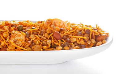 Hot spicy NavRatan snacks in a white ceramic oval bowl, made with red chili, peanuts, corn flakes, etc. Pile of Indian spicy snacks (Namkeen), under backlight, side view, against the white background.