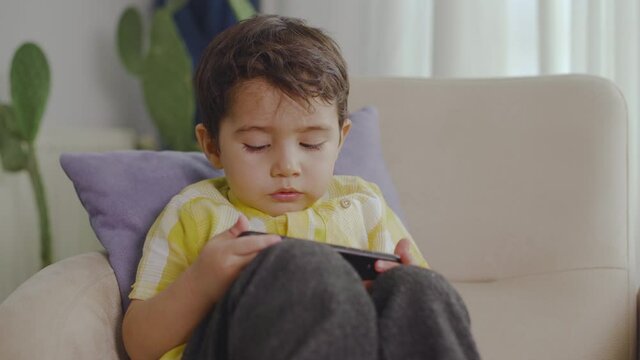 Boy sitting on sofa watching cartoons on the phone.
