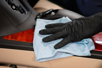 Close up of car wash worker wearing protective gloves and cleaning car interior with a wipe