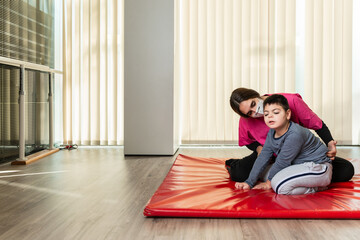 disabled child and physiotherapist on a red gymnastic mat doing exercises. pandemic mask protection