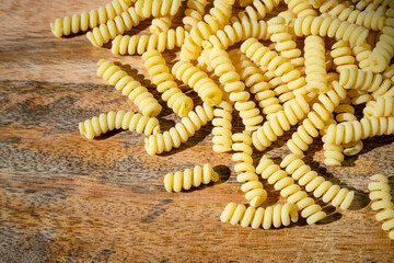 Uncooked curly pasta on wooden table background. Stack of traditional dry raw macaroni. Nobody