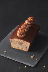 Chocolate-Covered Hazelnut Loaf Cake with Hazelnut Cream decorated with Whipped Chocolate Ganache and Praline Truffles, on a dark background.