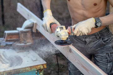 sanding the board with a hand-held power tool. Street, board clamped in a vise, small sawdust.