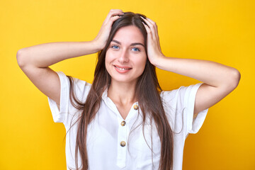 Portrait of brunette girl holding her head, smiling and rejoicing isolated on yellow background