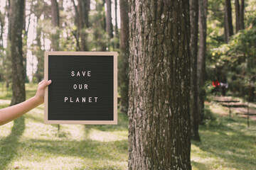 Hand holding a letter board that says save our planet on the forest, earth day concept.