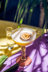 yellow tropical cocktail with passion fruit and shot on a background of tropical plant leaves and...