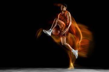 Fototapeta na wymiar Flying. Young arabian muscular basketball player in action, motion isolated on black background in mixed light. Concept of sport, movement, energy and dynamic, healthy lifestyle. Training, practicing.