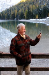 uomo anziano in riva al lago si fa un selfie