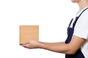 Side view of body of man in dark blue overalls and and a white T-shirt holding out a cardboard box in front of him and hands it over, isolated on white background. Delivery concept.