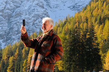 Uomo anziano in controluce si fa un selfie in vacanza in montagna