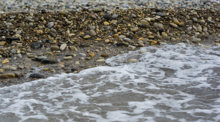 pebble stones on the sea beach, the rolling waves of the sea with foam