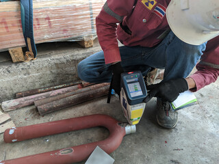 Worker inspect metal components of steel pipes with The Portable XRF Analyzer. XRF Gun is the...