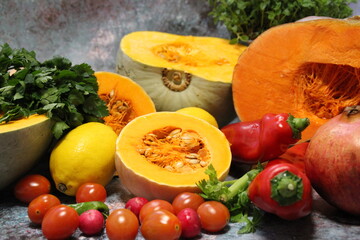 colorful vegetables, tomatoes, peppers, and large orange pumpkins cut in half, celery with fresh oregano and parsley in the background