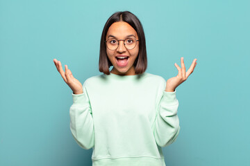 young hispanic woman feeling happy, excited, surprised or shocked, smiling and astonished at...