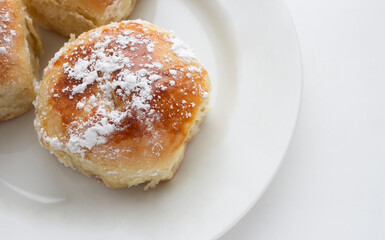 Delicious buns with powdered sugar on a white plate on a white background