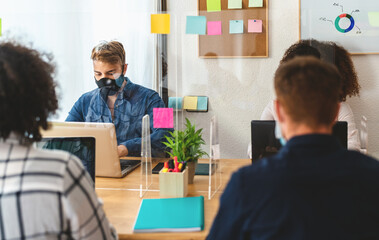 Young people in co-working creative space wearing surgical mask and keeping social distance to avoid corona virus spread - Health care and business technology concept