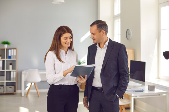 Business, Office, Communication, Teamwork Concept. Smiling Man And Woman Business People Office Workers Standing And Discussing Project Or Report Details Together Over Spacious Modern Workplace