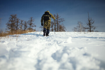 Extreme traveller with a backpack climbs on top of a snow-covered hill in frosty sunny day.