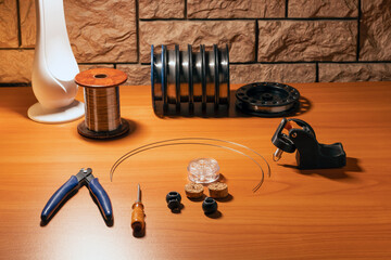 On the desktop there are tools and materials for making coils for electronic cigarettes-side cutters, a screwdriver, clips and coils with wire of different sections.