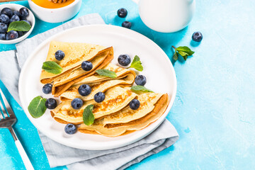 Crepes with blueberries and honey at blue table. Healthy breakfast or snack.