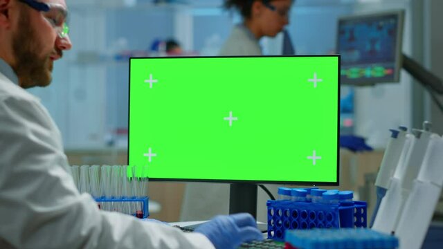 Man doctor working at pc with green screen in modern equipped lab analysing virus evolution. Team of microbiologists doing vaccine research writing on device with chroma key, isolated, mockup display.