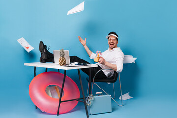 Perky businessman in suit and cap scatters graphics, enjoying tasty cocktail, sitting at table with...
