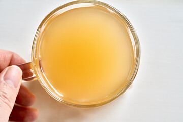 A cup of beef bone broth held by a hand on a white background