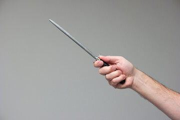 Caucasian male hand holding a steel knife sharpening rod isolated on gray background