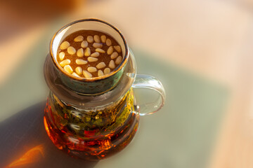 A saucer with honey and pine nuts is on the teapot A teapot with herbs is on the table on a sunny day.  The background is blurred