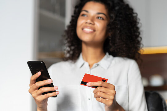 Blurred image of an African American teenage girl dreaming about future purchase, spending money from the first salary, holding credit card and mobile phone, close up of debit card and a cellphone