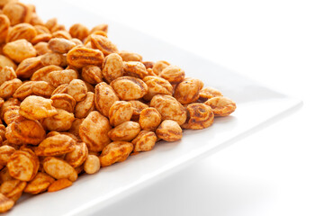 Roasted Crunchy Peanuts in a white ceramic square plate, made with peanuts. Pile of Indian spicy snacks (Namkeen), under backlight, side view, against the white background.
