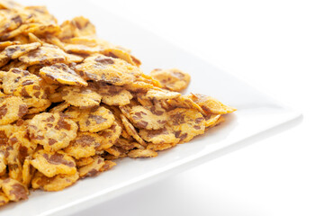Spicy Chana Jor Garam in a white ceramic square plate, made with air-fried Bengal Chickpea. Pile of Indian spicy snacks (Namkeen), under backlight, side view, against the white background.