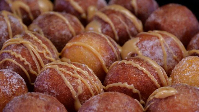 Cottage cheese doughnuts balls poured with caramel sweet sauce, rotating on a black background. Pouring caramel on a fresh baked quark cheese mini doughnut balls dusted in sugar.