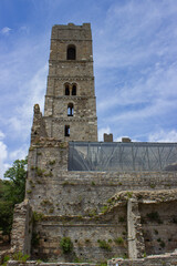 Detail of the ruins of Abbey of San Rabano, Alberese, Italy. Tower of the abbey against the sky with clouds. Ancient walls with the vegetation that has grown on it. Vertical image.