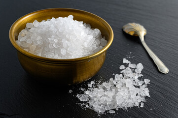 Bronze bowl of sea salt and small spoon on black background
