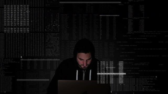Black hooded hacker in midst of computer code is frantically typing on keyboard of his system and infiltrating protected network. Computer crime, illegal access, bypassing the security firewall