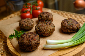 Homemade fried meatballs, served on wooden cutting board with tomatoes, onions and parsley