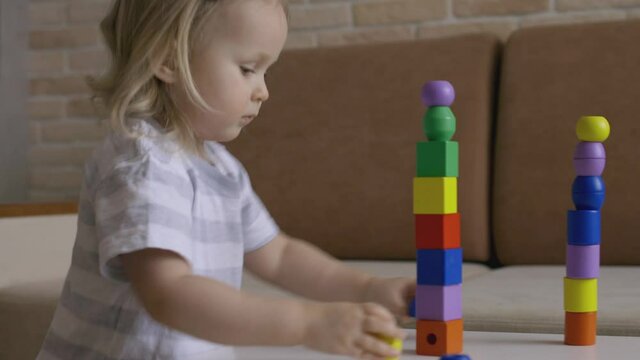 Little girl playing wooden geometrical figures on the table. Sorting rainbow cubes. Hand held Close Up Shot.
