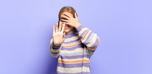blonde pretty woman covering face with hand and putting other hand up front to stop camera,...