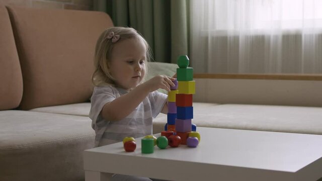 Little girl playing wooden geometrical figures on the table. Sorting rainbow cubes. Hand held Close Up Shot.
