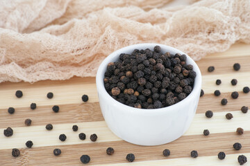 Fototapeta na wymiar Organic whole black peppercorns in a white bowl