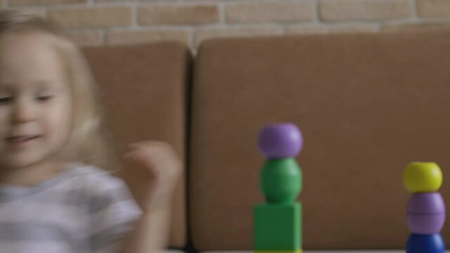 Little girl playing wooden geometrical figures on the table. Sorting rainbow cubes. Hand held Close Up Shot.