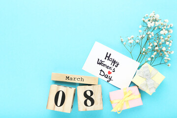 Wooden calendar cubes with gift boxes, gypsophila flowers and text Happy Womens Day on blue background